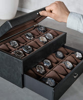 A person opens the TAWBURY Bayswater 24 Slot Watch Box with Drawer in Black/Grey, revealing multiple wristwatches arranged in rows on cushions—an absolute delight for watch enthusiasts.